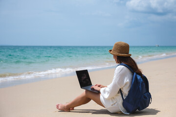 Wall Mural - a female traveler using and working on laptop computer while sitting on the beach