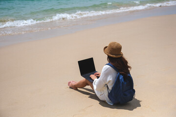 Wall Mural - a female traveler using and working on laptop computer while sitting on the beach