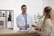 © New Africa - Patient giving medical insurance card to smiling receptionist at counter in clinic