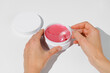 © Daryna  - Female hands are picking up a pink hydrogel patch with a transparent spatula from a white mockup jar on a white isolated background. Concept of beauty products, skin care under the eyes