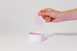 © Daryna  - With fingers, a woman picks up a pink hydrogel patch from a mockup white jar on a white isolated background. Hydrate, soothe, and fight dark circles and wrinkles for refreshed under-eye skin concept