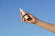 © Daryna  - Young woman's hand holding a glass nasal spray mockup on a blue isolated sky background. Concept of nasal cleansing, salt treatment, clean breathing
