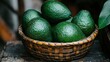 © STK - Close up view of several ripe green avocados in a rustic brown wicker basket, set against a dark background. The avocados are glistening, showing their textured skin.