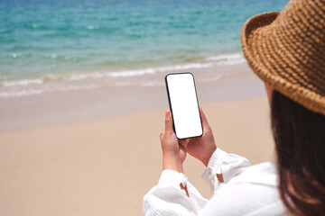 Wall Mural - mockup image of a woman holding mobile phone with blank desktop screen by the sea