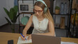 © Krakenimages.com - Young woman writing notes while working on laptop with headphones in modern office interior