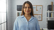 © Krakenimages.com - Young hispanic woman smiling confidently in a modern office environment with shelves and pinned documents in the background