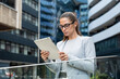 © Srdjan - Portrait of a successful business woman using digital tablet in front of modern business building. Businessperson office worker design professional occupation, innovative work outside of workspace.