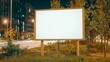 © Pojjanee - Billboard at Night: A blank billboard stands prominently at the edge of a road, illuminated by streetlights under the night sky, providing ample space for advertisement or a message in urban setting.
