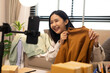 © Somdetmeaow - A woman is holding two boxes and smiling. She is sitting in front of a laptop. The boxes are brown and appear to be gifts. The woman seems happy and excited about the boxes