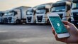 © thenort - Hand holding smartphone displaying GPS tracking app with semi-trucks in background.