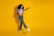 © deagreez - Young trendy girl with curly hair enjoying popcorn and pointing excitedly against a vibrant yellow backdrop