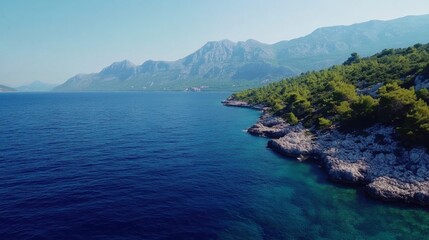 Aufkleber - Aerial view of the blue sea and rocky coastline with green trees, mountains in the background, cinematic.