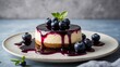 © Toni DiSalvo - Round cheesecake with blueberry syrup topping and fresh blueberries garnish on a white plate with a simple gray background
