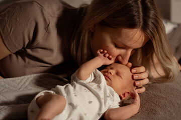 Aufkleber - Mother lovingly kisses her newborn baby while resting together in a cozy indoor space during the evening hours