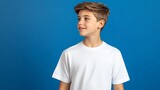Young boy with a white t-shirt looks sideways with a smile on a blue background
