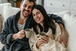 © La Famiglia - Happy couple wearing bathrobes relaxing on sofa and drinking coffee