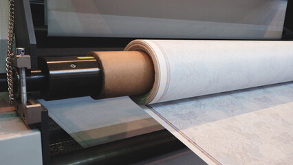 Poster - A roll of paper is being fed through a industrial printer machine. The roll is white and the machine is black