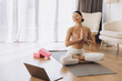 © anatoliycherkas - Woman practicing yoga online using laptop at home