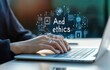 © Thinkinfinity - Close up of hands typing on a laptop keyboard, with glowing icons and the words And ethics floating above. The image is softly lit with a blurred