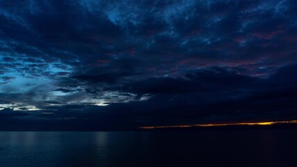 Wall Mural - dramatic clouds over tranquil sea water at sunset near a coastal location, time lapse 4k