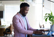© Wavebreak Media - African American man in pink blazer typing on laptop at modern office desk