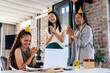 © Wavebreak Media - Diverse female colleagues celebrating with party hats and gifts in modern office setting
