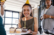 © Wavebreak Media - Smiling woman holding birthday cupcakes with candle at office celebration