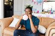 © Wavebreak Media - Baby shower, African American man blowing up balloon on couch at home party, looking cheerful