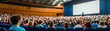 © taweesak - Engaged audience attentively watching male speaker in lecture hall with large screen displaying informative content