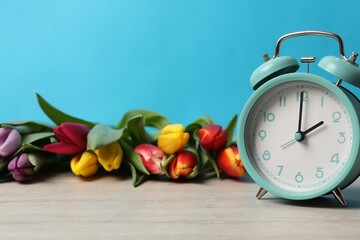 Poster - Spring time. Alarm clock and beautiful tulips on wooden table against light blue background