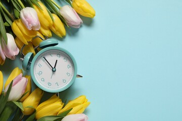 Poster - Spring time. Alarm clock and beautiful tulips on light blue background, flat lay. Space for text