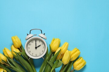 Poster - Spring time. Alarm clock and beautiful tulips on light blue background, flat lay. Space for text