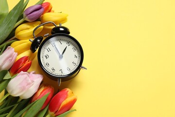 Poster - Spring time. Alarm clock and beautiful tulips on yellow background, flat lay. Space for text