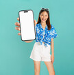 © sitthiphong - Portrait of young Asian woman in summer wearing floral shirt holding smartphone mockup of blank screen and smiling on blue background.
