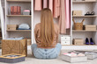 © Pixel-Shot - Beautiful young woman with clean clothes in different organizers sitting at wardrobe, back view