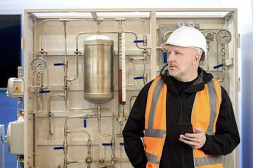 Poster - man engineer near boiler equipment. reservoirs tubes for home heating. man engineer holding phone. i