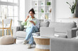 © Pixel-Shot - Young African-American woman drinking coffee on sofa at home