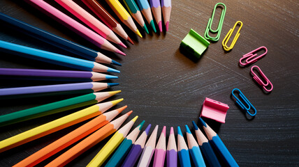 Poster - Colored pencils arranged in a semicircle on a dark surface, with colorful paperclips creating free space for text or logo, suggesting creativity and education