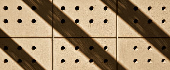 Aufkleber - Beige square panels with circular perforations, angled sunlight casting diagonal shadows, creating a geometric pattern, showcasing a modern architectural texture