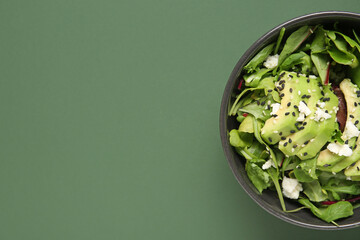 Wall Mural - Bowl of tasty avocado salad with mozzarella cheese and sesame seeds on green background