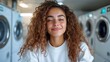 ©  Shomixer - A happy young woman with curly hair smiles in a modern laundry room, exuding positivity and joy as she enjoys her surroundings and appreciates everyday life’s simple pleasures.