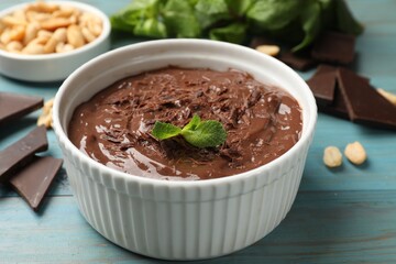 Wall Mural - tasty chocolate pudding in bowl and ingredients on light blue wooden table, closeup