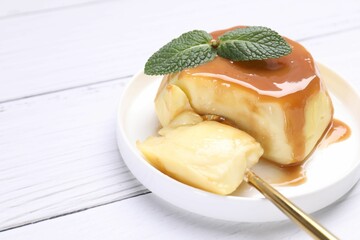 Wall Mural - delicious pudding with caramel sauce and mint served on white wooden table, closeup