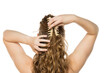 © vladimirfloyd - Rear view of young woman placing beige claw clip in her long wavy blonde hair, demonstrating half-up hairstyling process against white background