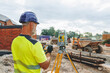 © Iryna - Builder engineer operating surveying equipment on a building site with machinery in the background