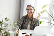 © shurkin_son - Selective focus on cheerful happy aged female freelance worker in glasses working from home, sitting at table with laptop, smartphone and cup of coffee, making notes while looking at camera with laugh