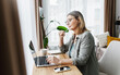 © shurkin_son - Side view indoor portrait of smart intelligent senior lady working on laptop sitting at table with pen in hand, aged female student studying online, making notes in notebook, looking at screen