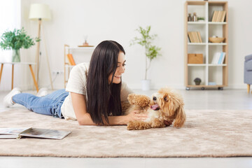 portrait of young happy smiling female owner playing with her little cute dog lying on floor in the 