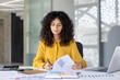 © Liubomir - Serious thinking female accountant doing paperwork inside office. Businesswoman recording data, preparing reports, filling out tax forms. Woman with documents and graphs with laptop.
