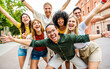 © Davide Angelini - Multicultural group of young people smiling at camera outdoors - Happy friends having fun on city street - Youth community with diverse guys and girls hugging together